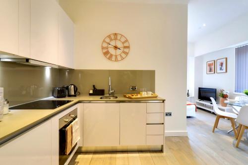 una cocina con armarios blancos y un reloj en la pared en La Casa Suites Slough, en Slough