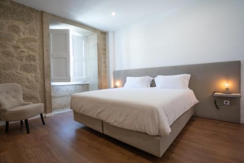 a bedroom with a large white bed and a chair at Solar Valadim - serviced apartments in Castelo Branco