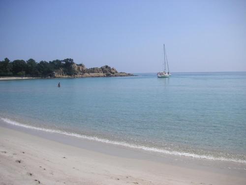 a sail boat in the water next to a beach at La Solenzara hôtel - 3 Etoiles Supérieur - Appartement & SPA in Sari Solenzara