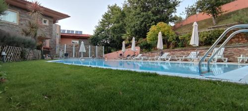 a swimming pool with chairs and umbrellas in a yard at Hotel Rural Quinta da Conchada in Aguieira