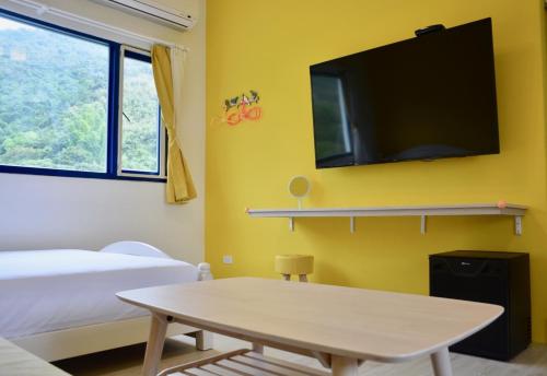 a room with a table and a tv on a yellow wall at Blue and White Style Holiday B&B in Guanshan