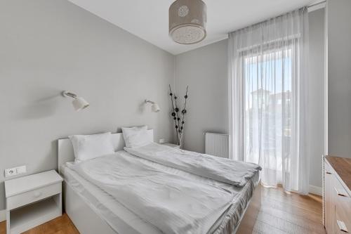a white bedroom with a bed and a window at Luxury Bianco Apartament in Sopot