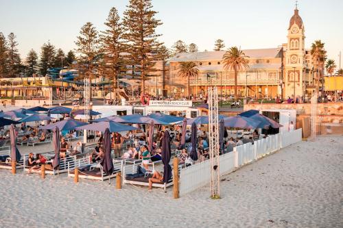 a group of people sitting under umbrellas on the beach at Beachside Luxury Apartments One & Two Bedroom in Beachfront Oaks Pier Building in Glenelg