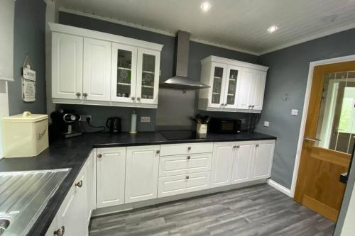 a kitchen with white cabinets and black counter tops at Tigh na h'aibhne in Broadford
