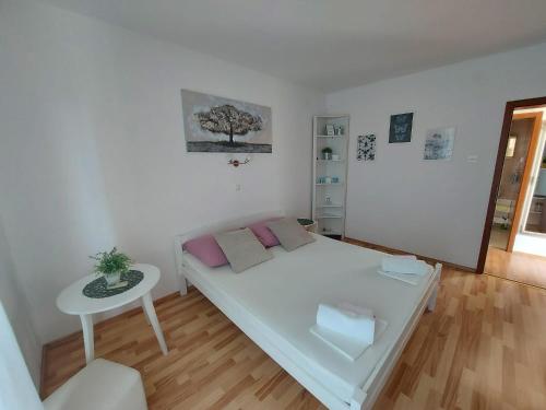 a white bedroom with a bed and a table at Rab - Apartman Matea in Rab