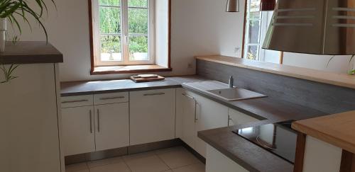 une cuisine avec des armoires blanches et un évier dans l'établissement La Maison près du ruisseau, à Fenioux