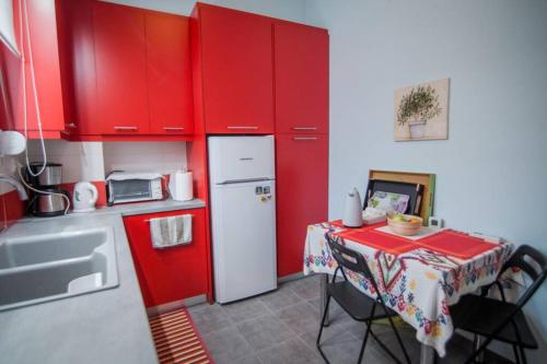 a red kitchen with a table and a white refrigerator at ΑΝΑΚΑΙΝΙΣΜΕΝΗ ΜΟΝΟΚΑΤΟΙΚΙΑ στο κέντρο της πόλης με κήπο in Mesolongion