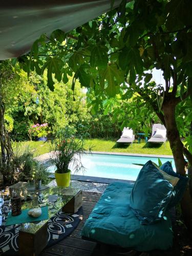 un canapé bleu assis sous un arbre à côté d'une piscine dans l'établissement La Maison D'ayona, à Herrlisheim-près-Colmar