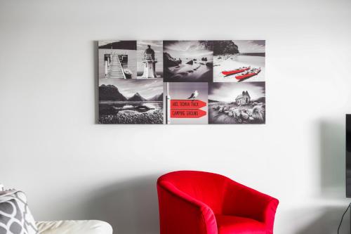 a red chair in a living room with a picture on the wall at Auckland Waterfront Serviced Apartments on Prince's Wharf in Auckland