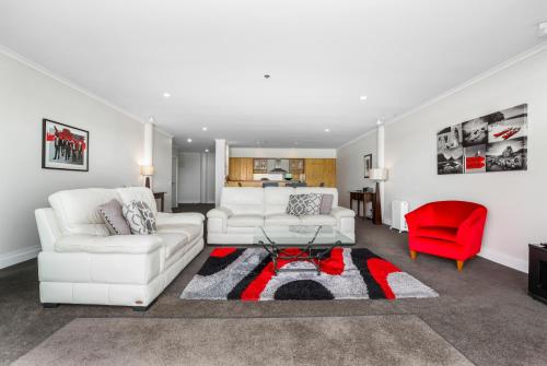 a living room with two white couches and a red chair at Auckland Waterfront Serviced Apartments on Prince's Wharf in Auckland