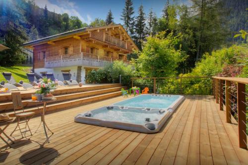 a deck with a hot tub and a house at Chalet Le Mousqueton - OVO Network in La Clusaz