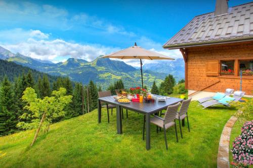 a table with an umbrella on a lawn with mountains at Chalet de Paul et Marie - OVO Network in Manigod