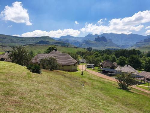 a house on a hill with mountains in the background at Fairways Holiday Accommodation in Drakensberg Garden