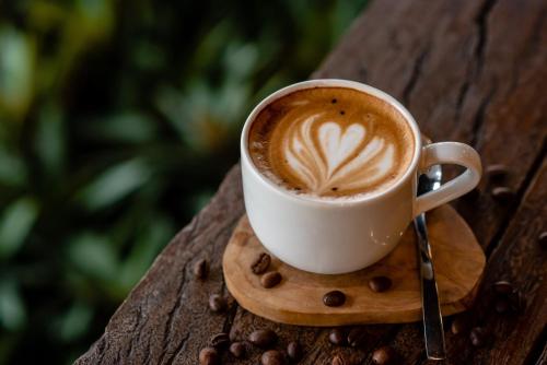 a cup of coffee sitting on a table with coffee beans at The Rooms Apartment Bali by ARM Hospitality in Denpasar