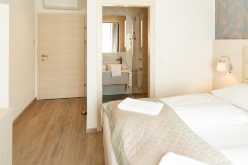 a white bedroom with a bed and a bathroom at Hotel Rösch in Klagenfurt