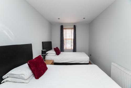 two beds in a room with white walls and red pillows at The New Mill Apartments in Newcastle upon Tyne