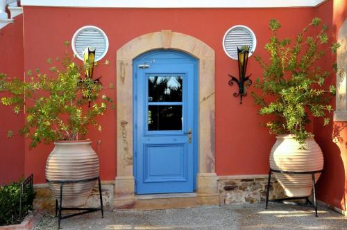 una puerta azul en una casa roja con dos vasijas grandes en Sourediko, en Kambos