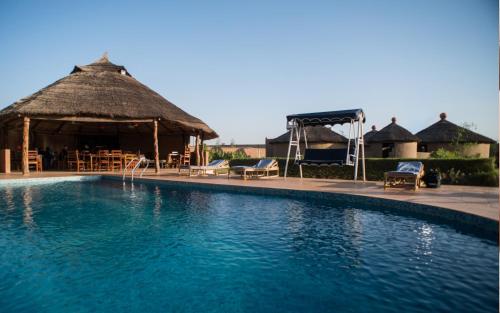 a large swimming pool with a thatch hut and chairs at Le Grand Calao in Ouagadougou