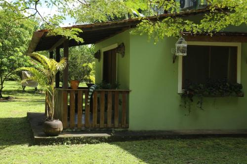 una casa verde con un porche y una planta en Sítio Pássaro Ímpar - Para pousar e repousar, en Curuçá