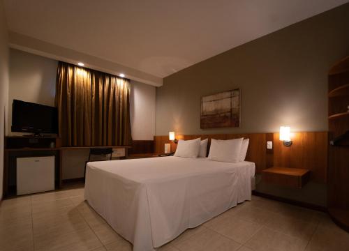 um quarto com uma cama branca e uma televisão em Executive Inn Hotel em Uberlândia