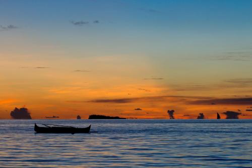 a boat sitting in the water at sunset at Anjiamarango Beach Resort in Nosy Be