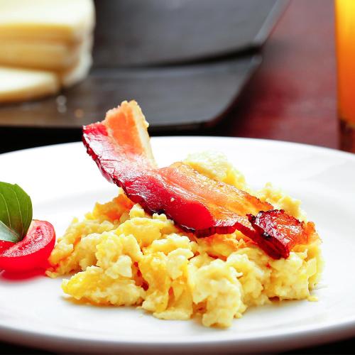 un piatto bianco con una colazione a base di uova e pancetta di Fratele Business Hotel a Patos de Minas