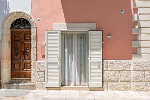 a door with white shutters next to a pink building at La Vite Bianca in Polignano a Mare