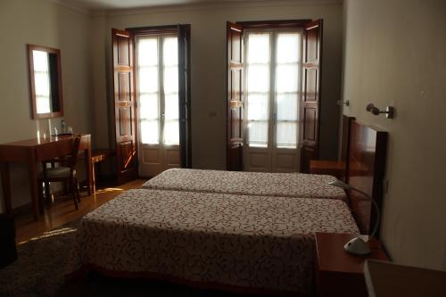 a bedroom with two beds and a table and windows at Guesthouse Muralhas do Mino in Monção
