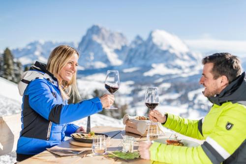 a man and woman sitting at a table with wine glasses at Hotel Jägerhof in Colfosco