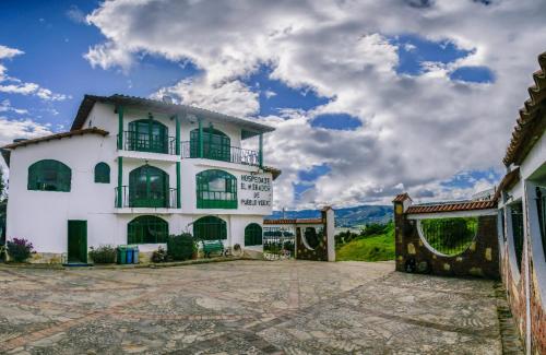 a white building with green windows and a cloudy sky at Hospedaje Mirador de Pueblo viejo in Guatavita