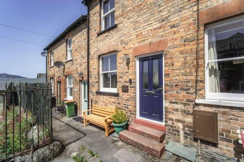 a brick house with a blue door and a wooden bench at Isabel Cottage in Keswick