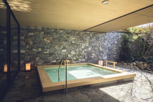 a hot tub in a patio with a stone wall at Tokyu Stay Hida Takayama Musubinoyu in Takayama