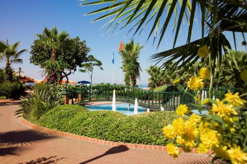 a swimming pool in a garden with yellow flowers at Riviera Hotel & Spa in Alanya