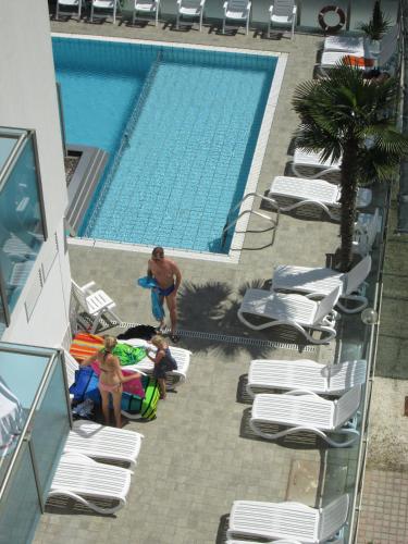 a swimming pool with chaise lounge chairs and a man and two girls standing at Appartamenti Katja in Bibione