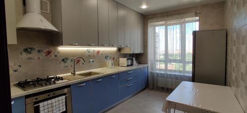 eine Küche mit blauen Schränken, einem Waschbecken und einem Fenster in der Unterkunft Сучасні апартаменти in Luzk