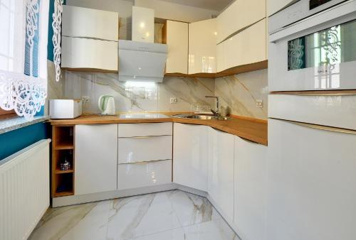 biała kuchnia z białymi szafkami i zlewem w obiekcie Apartament Szmaragdowy w mieście Karpacz