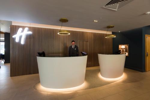 a man standing at a counter in a lobby at Holiday Inn Cambridge by IHG in Cambridge
