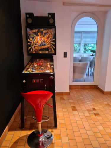 a pinball machine with a red stool in a room at La coudraie votre maison de vacances en famille in Daumeray