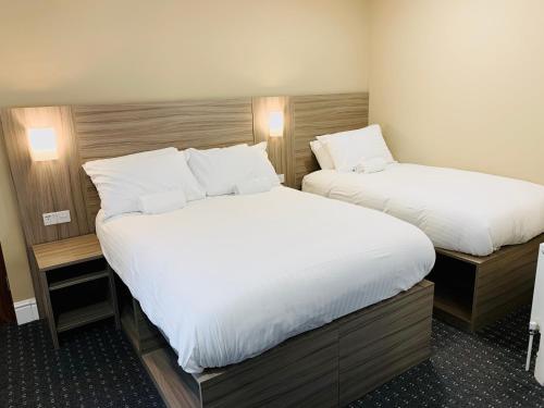two beds in a hotel room with white sheets at De Regency Style Hotel in Redditch