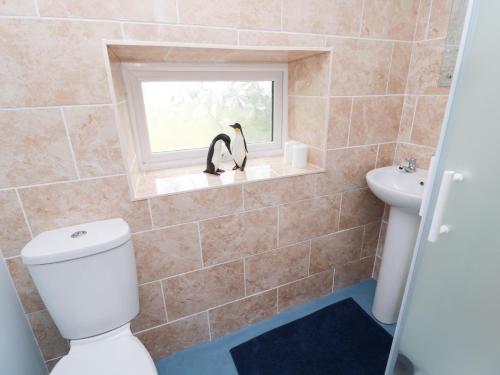a bathroom with a toilet and a window with two penguins at 1 Roddam Rigg Cottage in Alnwick