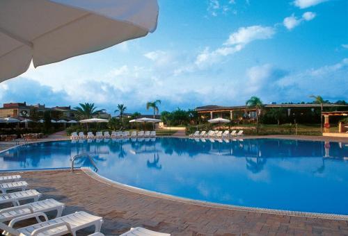 una grande piscina con sedie bianche e ombrelloni di iGV Club Santagiusta a Castiadas