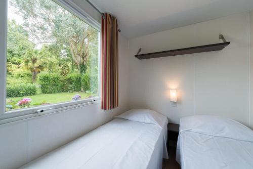 two beds in a room with a window at L'Orangerie de Lanniron - Mobil-Home O'HARA privilège - 3 chambres - 6 pers in Quimper
