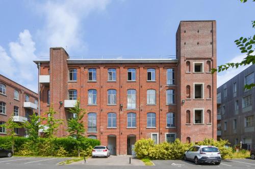 un grand bâtiment en briques avec des voitures garées dans un parking dans l'établissement Beautiful loft in a former factory in Tourcoing - Welkeys, à Tourcoing