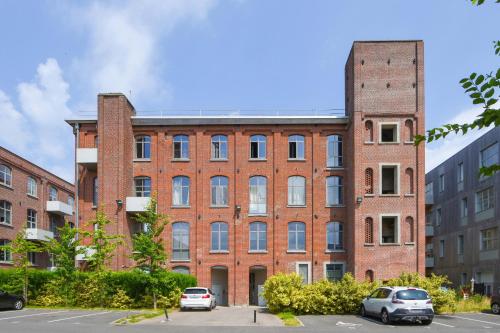 un gran edificio de ladrillo con coches aparcados en un aparcamiento en Beautiful loft in a former factory in Tourcoing - Welkeys, en Tourcoing