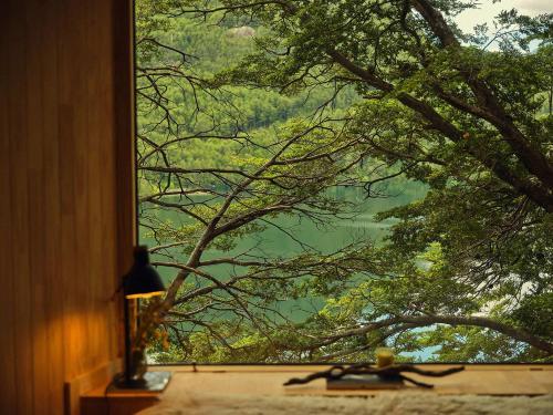 a window with a view of a lake through the trees at MA PU LODGE Futaleufu in Futaleufú