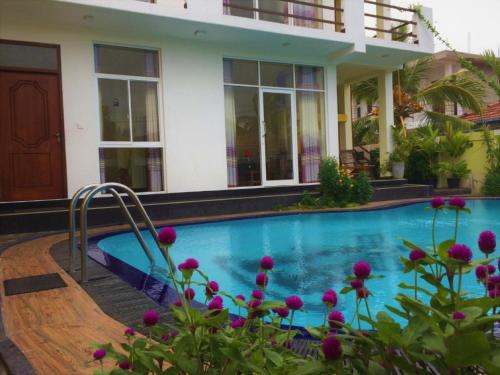 a swimming pool in front of a house with purple flowers at Romeo and Juliet Guest House in Negombo
