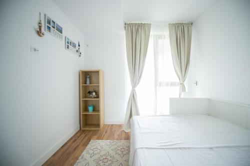 ein weißes Schlafzimmer mit einem Bett und einem Fenster in der Unterkunft Apartel Emerald Bay in Mamaia Nord – Năvodari