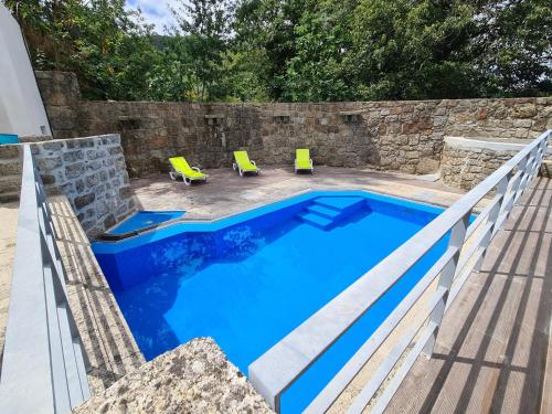 a swimming pool with a stone wall and two yellow chairs at Quinta do Avô - Casa de Campo in Terras de Bouro