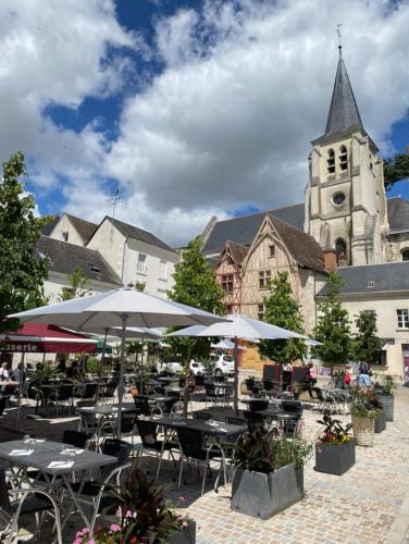 an outdoor cafe with tables and umbrellas in front of a church at La Chancellerie in Montrichard