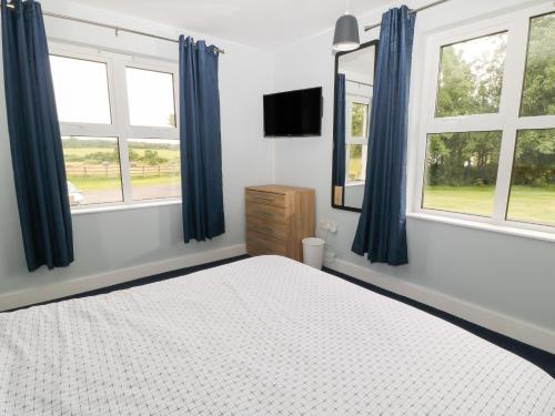 a bedroom with blue curtains and a bed and two windows at Cherry Tree Cottage in Bude